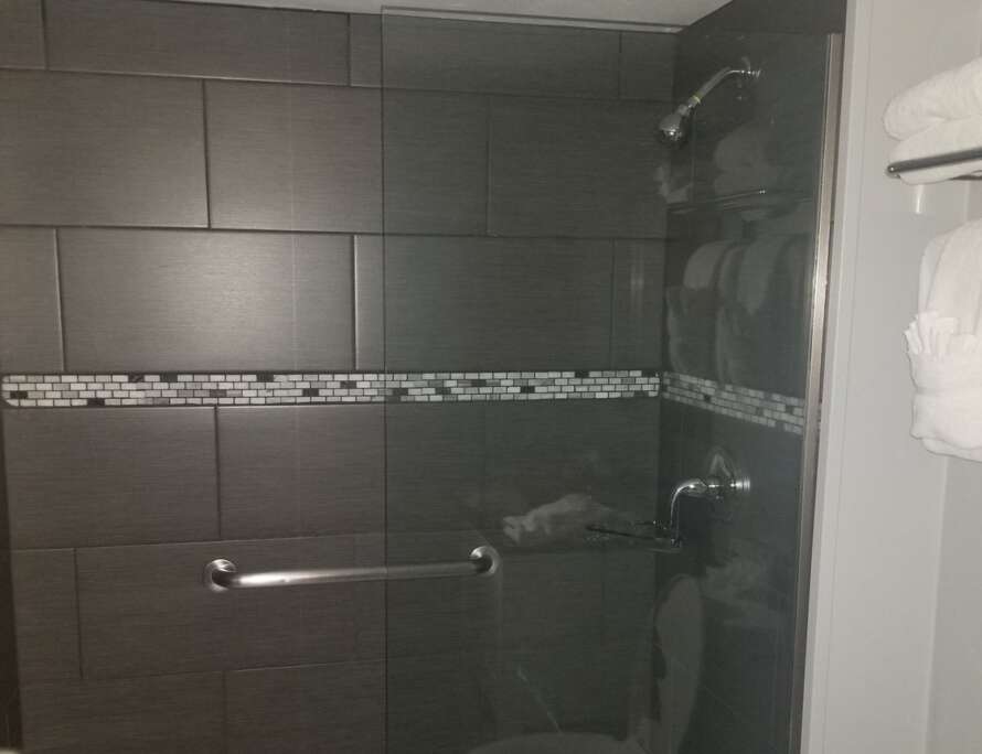 Dark grey tile shower with a mosaic accent band in a Kansas City home after a Bathroom Bidders grout cleaning and sealing