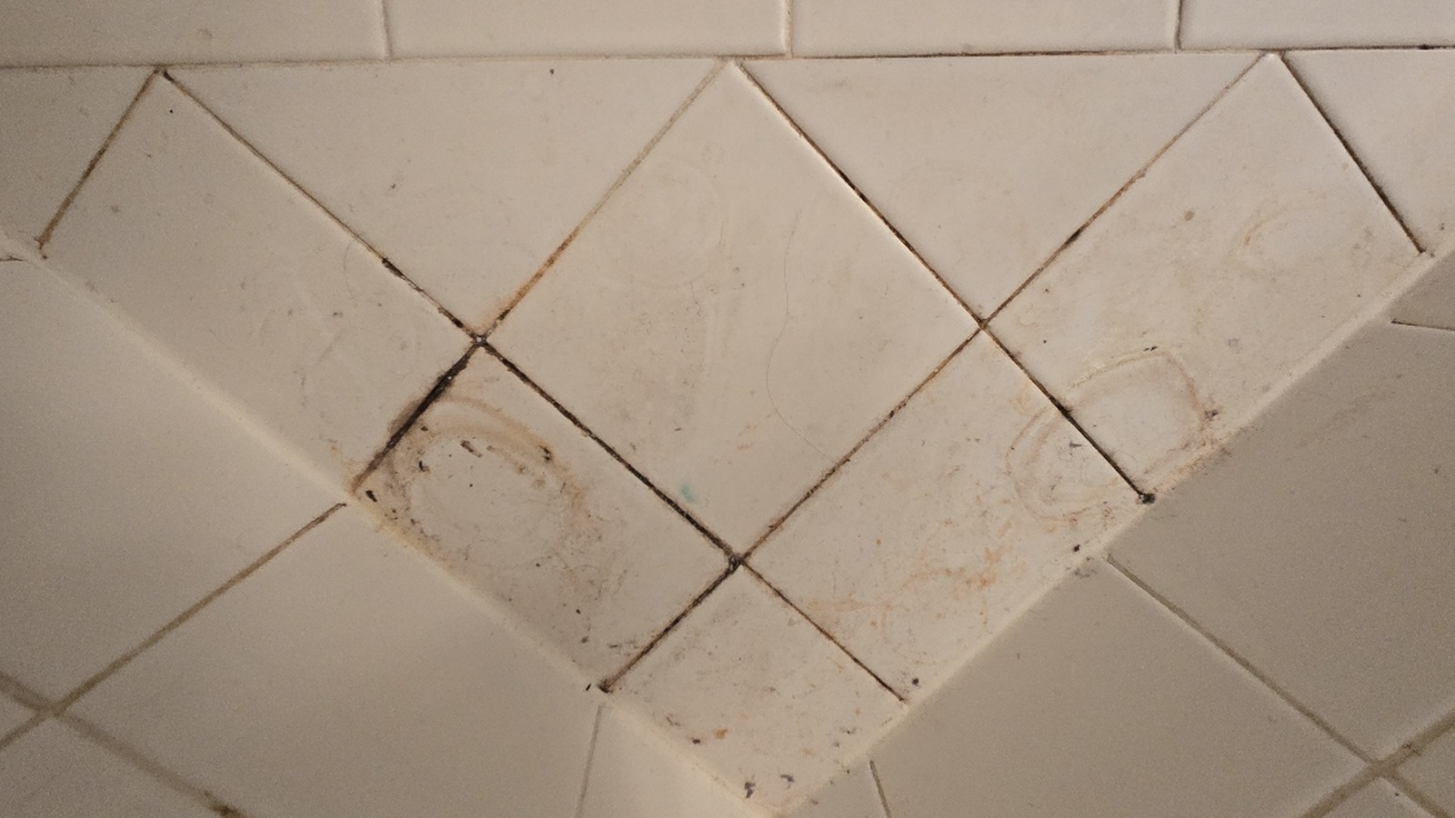 Darkened grout lines and orange mineral staining on white diamond set tile in a Kansas City shower before cleaning