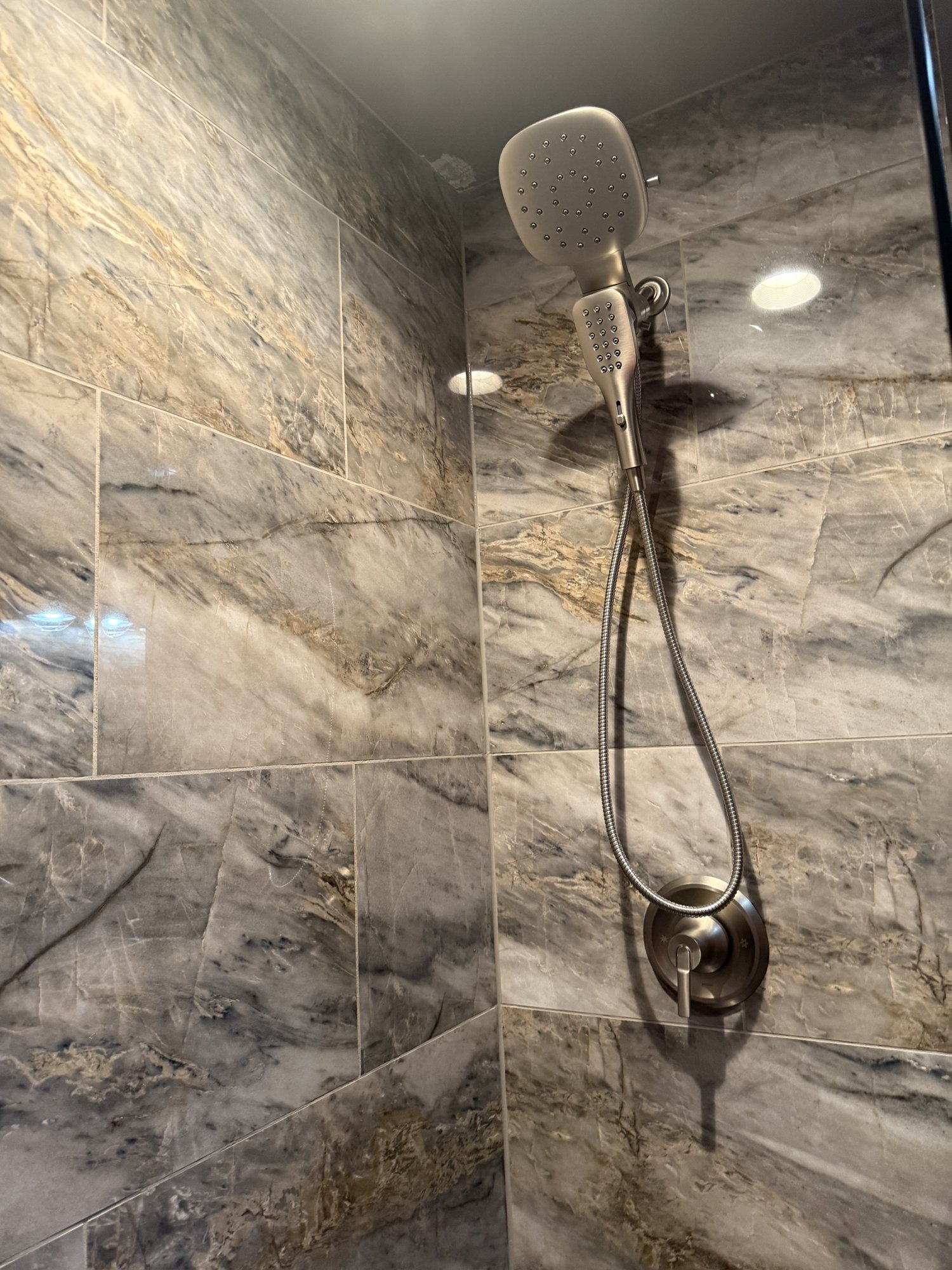 Marble-look wall tile with a brushed nickel handheld shower and valve