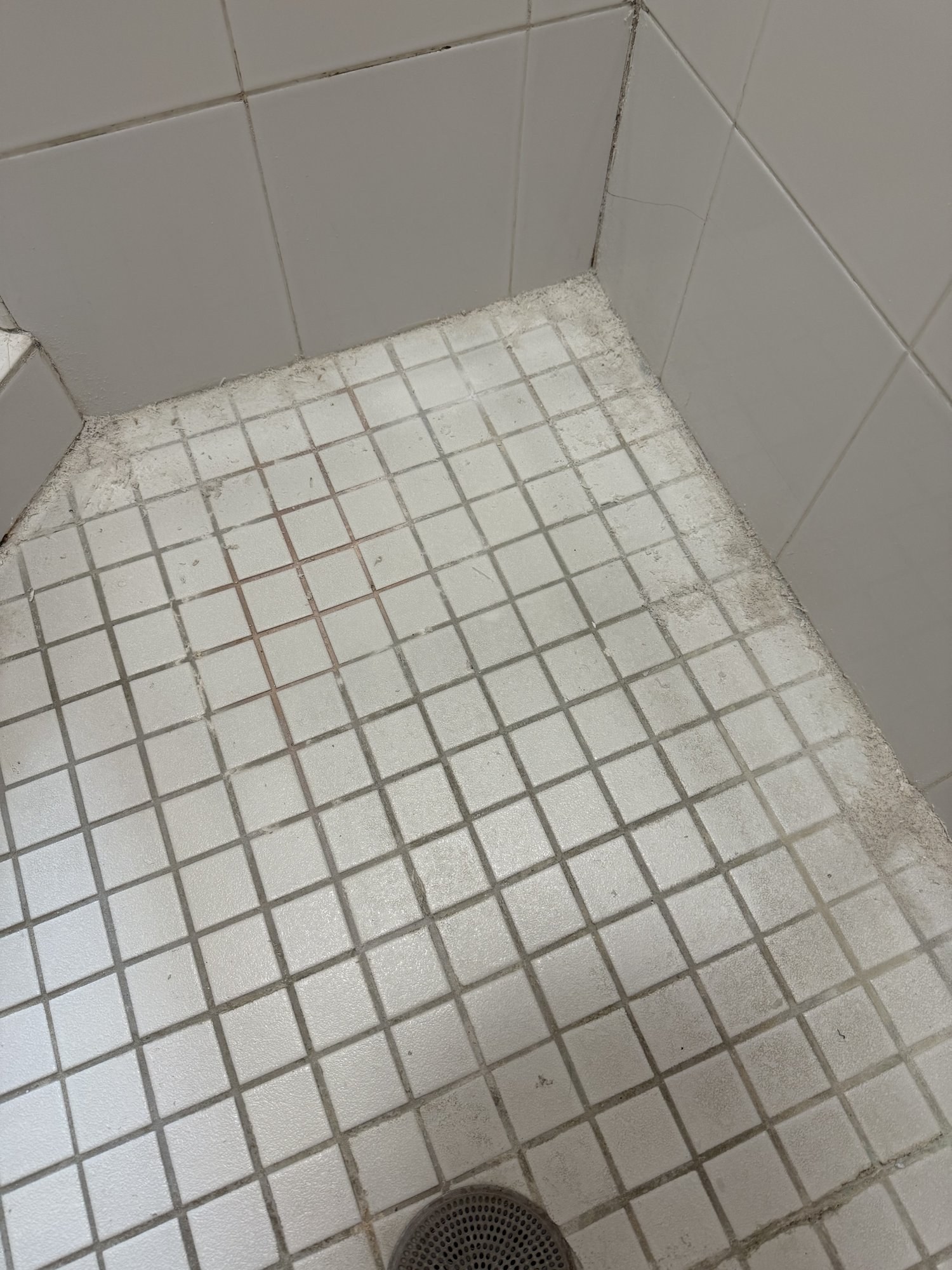 Before: stained grout and buildup on a white mosaic shower floor in Prairie Village